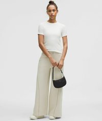 Camiseta blanca de manga corta combinada con pantalones de chándal anchos beige, con cordón y costuras visibles. Un pequeño bolso negro completa el look.