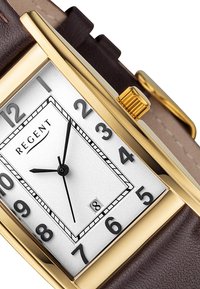 Montre rectangulaire en ton or avec un cadran blanc, des chiffres arabes noirs et un affichage de la date. Bracelet en cuir marron avec finition texturée.