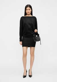 Μαύρο σατέν φόρεμα με μακριά μανίκια, εφαρμοστή φούστα και στρογγυλή λαιμόκοψη. Συνδυάζεται με μια μαύρη τσάντα με υφή και ψηλοτάκουνα παπούτσια με μυτερή μύτη.