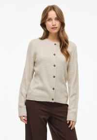 Cárdigan beige de canalé con cuello redondo, cierre delantero de botones y mangas largas, que presenta botones de madera natural y una textura suave.