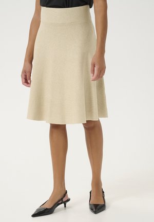 Jupe beige jusqu'aux genoux avec une taille ajustée, tissu texturé, design évasé. Associée à des escarpins à talons aigus noirs.