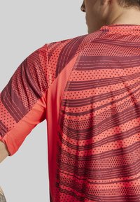 Camisa atlética roja con un patrón texturizado que incluye líneas y puntos. Fabricada con una tela transpirable con un acabado suave y un corte relajado.
