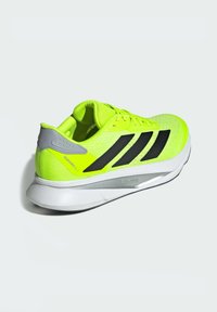 Neon yellow athletic shoe with black stripes, mesh upper, padded collar, and grey accents on heel, featuring a white, textured sole.