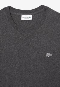 T-shirt grigio carbone realizzato in morbido tessuto, con un design a colletto rotondo e un piccolo logo bianco di Lacoste sul lato sinistro del petto.