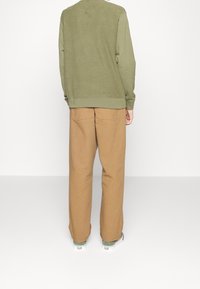 Sweatshirt vert olive avec un col rond et un ourlet côtelé, associé à un pantalon large beige avec deux poches arrière.