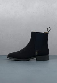 Bottine en cuir noir avec panneaux latéraux élastiques, talon bas, languette de tirage et marquage GANT sur le côté, sur un fond neutre.
