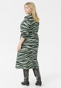 Abito a stampa zebra verde con maniche lunghe, vita stretta e spacco laterale, abbinato a stivali neri con ricami argentati.