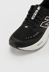 Chaussure de sport noire avec une tige en mesh, des accents blancs contrastants, une semelle lisse portant l'étiquette "FRESH FOAM" et un design à bout arrondi.