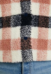 Fleece bunda s kostkovaným vzorem v broskvové, krémové, černé a šedé barvě. Výrazné detaily knoflíků a měkká, strukturovaná tkanina.
