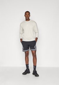 Felpa grigia con logo, abbinata a pantaloni sportivi neri con strisce bianche ai lati. Le sneakers nere e le calze scure completano l'outfit.