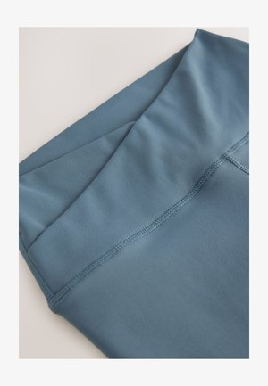 Blauwe atletische stof met een gladde textuur, netjes opgevouwen aan de bovenkant. Heeft een vlakke naad langs de rand, met een eenvoudig ontwerp.