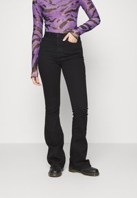 Jeans neri a palazzo con una texture liscia, vita alta e design classico a cinque tasche, abbinati a stivali neri con lacci.