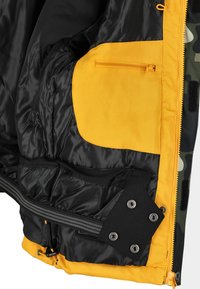Svart innervaddering av en jacka med en stor gul ficka. Har en dragkedjeficka, ribbad elastisk band och metaltryckknappar.