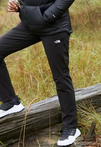 Svart utomhusbyxor med stretchtyg, med en liten vit logotyp på låret, kombinerat med svart-vita sportskor.