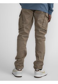 Tan cargobroeken met meerdere zijzakken, een ontspannen pasvorm en duurzaam materiaal. Gepaard met grijze Nike-schoenen met een witte en bruine zool.