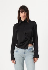 Juodos satino marškiniai su ilgomis rankovėmis, turintys įvyniojimo dizainą, apykaklę ir surištą liemenį. Įtrauktas mažas logotipas ant apvado ir platėjantys rankogaliai.