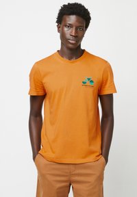 Korte mouwen oranje katoenen T-shirt met een geborduurd ontwerp van een blauwe en groene fiets en de tekst "ALTIJD FIETSEN" op de borst.