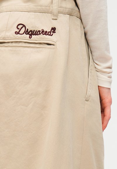 Μπεζ ένδυμα με ομαλή υφή, διακοσμημένο με κεντημένο λογότυπο "Dsquared2" σε μπορντό απόχρωση και λεπτομέρεια πλαϊνής τσέπης.