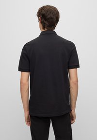 Black polo shirt with short sleeves, ribbed collar, and a straight hem. Smooth texture, minimalistic design, and no visible patterns or accents.