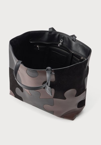Grand sac fourre-tout avec design de pièces de puzzle en noir, gris et marron, poignées en cuir, et intérieur visible avec poches zippées et clip pour clés.