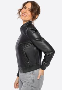 Černá kožená bomber bunda s žebrovanými manžetami a pasem, s předním zipem a bočními kapsami. Hladká textura a přiléhavý střih.