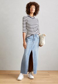 Pruhovaná košile s dlouhým rukávem a nařasenými rameny, spárovaná s maxi sukní z světle modrého denimu s rozparkem a roztrhaným lemem. Bílé tenisky a béžová kabelka.