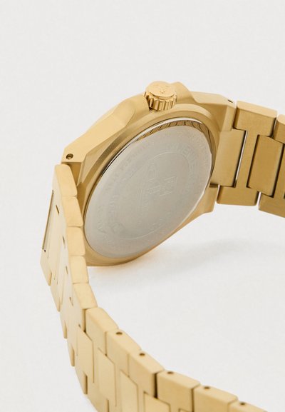 Relógio de pulso em metal dourado com bracelete de elos, caixa redonda, coroa texturizada e traseira gravada. Design limpo com uma superfície refletora.