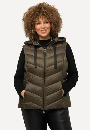 Olijfgroen gewatteerd vest met een capuchon, uitgerust met chevron-quilting, een rits aan de voorkant en zwarte verstelbare banden. Draag het over een zwarte trui.