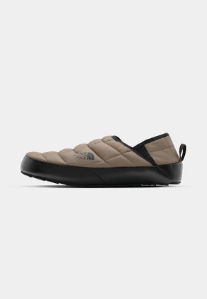 Beige quiltet slip-on sko med en sort gummisål, polstret overdel og stikningsdetalje. Har et trækstrop for nem påtagning.