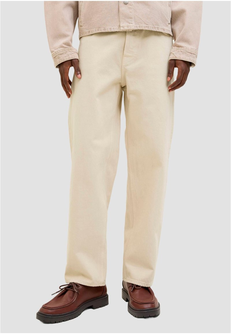 Bež široke hlače širokih nogavica izrađene od čvrste tkanine, s glatkom teksturom i čistim završetkom. Uparene s smeđim kožnim cipelama na vezanje.