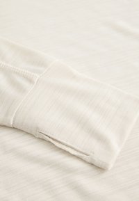 Beige long-sleeve shirt with a textured finish. Features a cuff with a clean hem and a subtle stripe pattern. Soft, lightweight fabric.