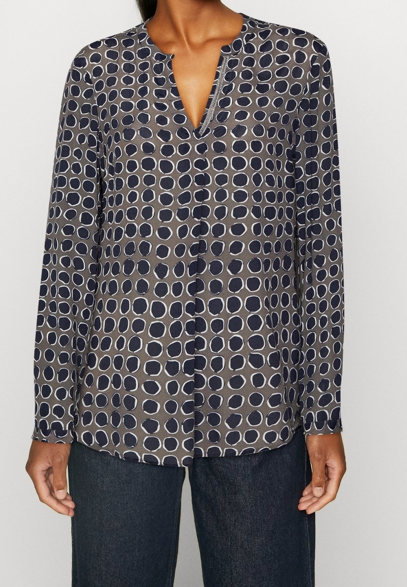 Långärmad, marinblå blus med v-ringning och cirkulärt vitt prickmönster. Mjuk tyg, något lös passform, knäppt fram för stängning.