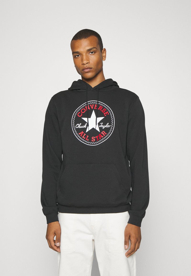 Czarna bluza z kapturem wykonana z bawełny z przednią kieszenią kangurką. Posiada okrągły grafikę w czerwono-białych kolorach z gwiazdą i napisem "Converse All Star".
