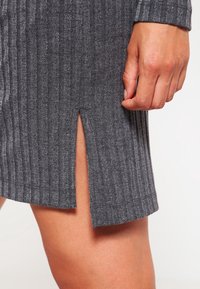 Abito grigio a coste con spacco laterale, che mette in mostra linee verticali e una morbida texture. Il tessuto sembra elastico e aderente.