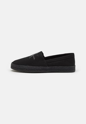 Zapato espadrille negro con parte superior de lona y suela de yute trenzado. Presenta un logo bordado en el costado y un diseño sin cordones.