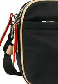 Schwarze Nylon-Tasche mit beigefarbenen Akzenten, ausgestattet mit einem Reißverschluss oben, orangefarbenen Hardware-Elementen und einer Fronttasche. Strukturiert für Grip und Langlebigkeit.