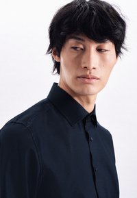 Camicia blu navy con colletto strutturato e tessuto testurizzato. Presenta una vestibilità slim con una leggera lucentezza e untaglio dritto.