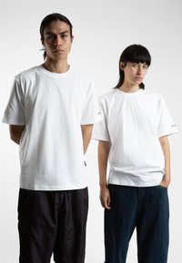 Two models wearing white cotton t-shirts. The t-shirts have a classic crew neck design and short sleeves. One model has dark pants, the other denim.