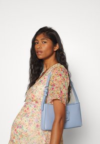 Bolsa de pele azul com formato retangular, alça ajustável e aba frontal. A bolsa tem uma textura suave e hardware minimalista.