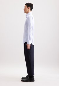 Camicia azzurro chiaro a maniche lunghe con polsini a bottone, abbinata a pantaloni a gamba larga blu navy e scarpe in pelle nere. Tessuto liscio e vestibilità su misura.