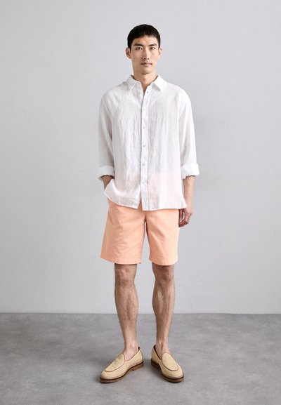 Weißes Leinenhemd mit langen Ärmeln, hellpfirsichfarbene Shorts und beige Slipper mit geflochtenen Details. Einfaches Design, lockere Passform.
