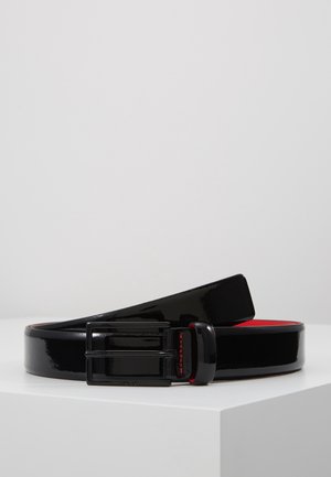 Black glossy leather belt with black rectangular buckle and red interior, placed coiled on a white surface.