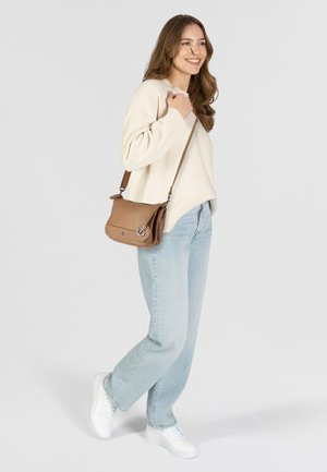 Borsa a tracolla in pelle color cuoio con patta magnetica, decorata con logo a forma di ancoraggio, cinturino regolabile, abbinata a un maglione crema e jeans azzurri chiari.