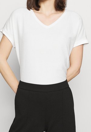 Witte V-hals T-shirt met opgerolde korte mouwen, met een zachte textuur en een ontspannen pasvorm, gecombineerd met zwarte, hooggetailleerde broek.