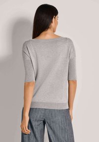 Grauer, kurzärmeliger Pullover mit weitem Ausschnitt und ribbeligem Saum. Der Stoff wirkt weich und leicht strukturiert. Kombiniert mit gestreiften Hosen.