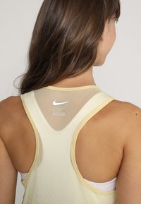 Camiseta deportiva de color amarillo claro con espalda de malla, que presenta un logo de Nike. La tela parece suave y tiene una textura liviana y transpirable.