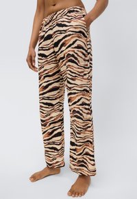 Pantalon de pyjama large à rayures marron et noires avec une taille élastique, des poches latérales et une texture de tissu douce et légère.