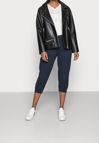 Zwarte leren motorjack met zilveren ritssluitingen, wit topje met kant, marineblauwe cropped broek en witte sneakers.