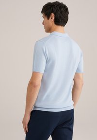 Polo de culoare albastru deschis, cu mânecă scurtă, dintr-un material tricotat fin, având un guler clasic și manșete ribbenate, prezentat din spate.