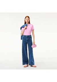 Maglietta polo rosa con maniche corte, abbinata a jeans blu a vita alta e a gamba larga. Gli accessori includono una borsa rosa chiaro e un giubbotto di jeans.